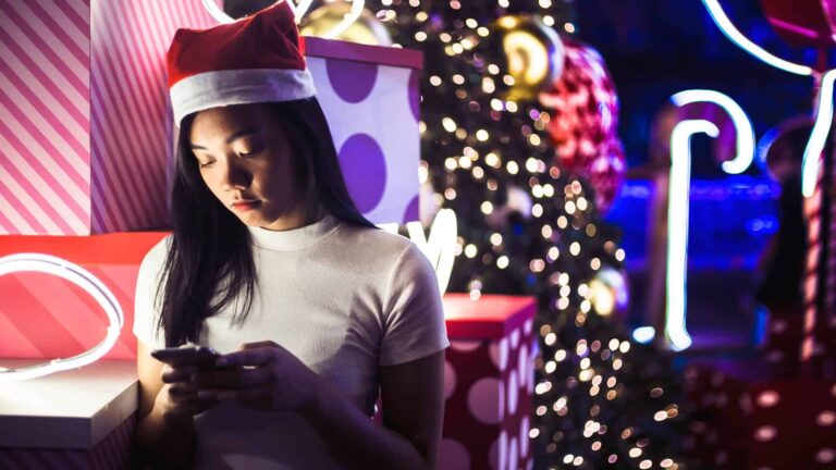 Mujer frente a un árbol de Navidad usando su móvil para la reconquista a tu pareja en festivos.